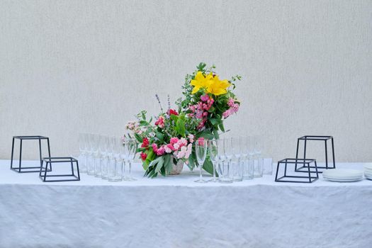 Decoration of events, close-up details of decor, catering. Table with white tablecloth glasses plates and flower arrangement in the garden outdoor