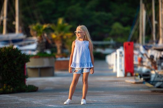 Portrait of a cute smiling little girl with glasses.A girl in shorts and a blue T-shirt at sunset by the sea.Turkey.