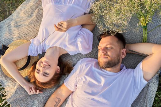 Portrait of beautiful happy couple in 30s 40s. Top view of smiling faces of man and woman lying together in sunset sunlight. Middle-aged people in love, relationship, relaxation, happiness, lifestyle