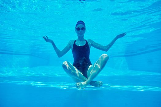 Young athletic woman sitting in lotus pose underwater in swimming pool.