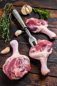 Fresh Raw Duck legs on meat fork with herbs. Dark wooden background. Top view.