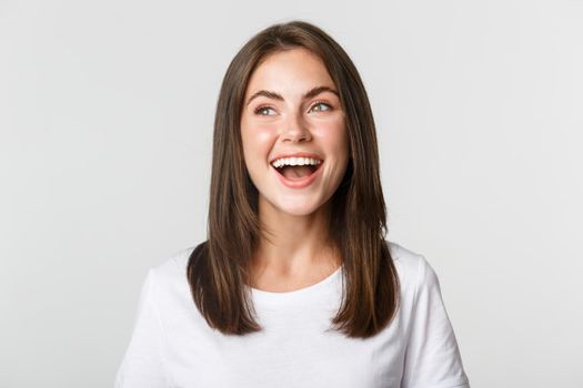 Close-up of joyful beautiful brunette girl looking upper left corner and laughing happy, white background.