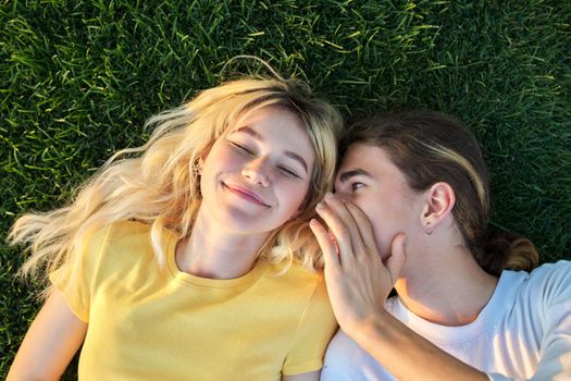 Happy couple of teenagers on green grass. Close-up of smiling faces of guy and girl 16, 17 years old, top view. Youth, adolescence, happiness, relationship, lifestyle, young people concept