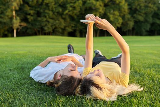 Happy couple of teenagers on green grass. Close-up of smiling faces of guy and girl 16, 17 years old, top view. Youth, adolescence, happiness, relationship, lifestyle, young people concept