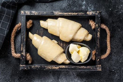 Raw fresh croissant in a wooden tray. Black background. Top view.