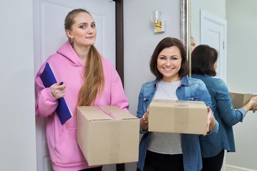 Delivery of goods, social services, post, home, lifestyle, online shopping. Two women with cardboard boxes near the front door of the house