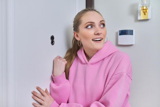 Young smiling woman standing near front door with peephole.