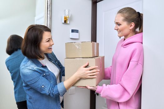 Online shopping delivery service, courier young woman with cardboard boxes near front door in apartment, adult woman buyer takes boxes