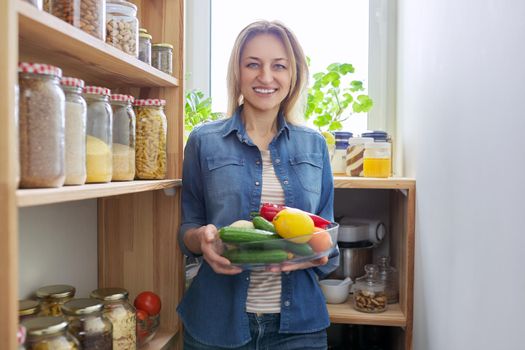 Portrait of middle-aged woman housewife in kitchen in pantry with bowl of vegetables in her hands. Female food blogger, healthy food, hobbies and leisure, eating at home concept