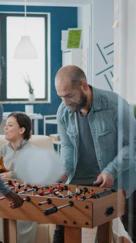 African american woman beating man at foosball game while enjoying after work drinks with workmates at office. Colleagues playing soccer at football table to have fun and entertainment.