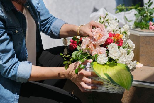 Female florist doing floral arrangement outdoors. Flower basket creation workflow.