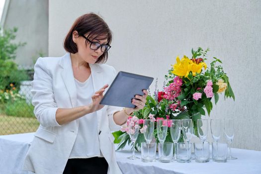 Organization of parties, ceremonies, professional woman event organizer with digital tablet, reserved holiday table decorated with flower arrangements. Female small business owner