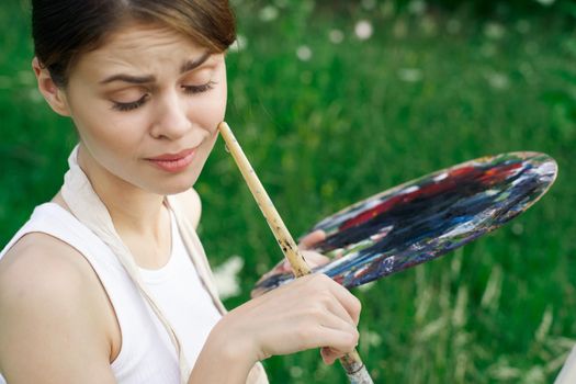 Woman in white dress with palette of paints on nature art drawing. High quality photo