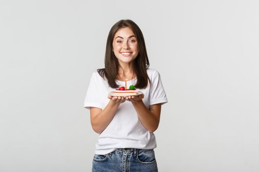 Excited attractive brunette b-day girl making wish on birthday cake, white background.