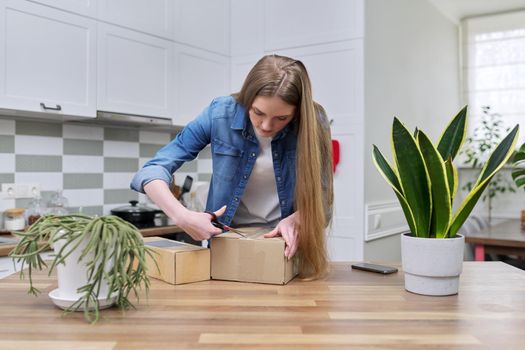 Young happy woman unpacking cardboard boxes, unboxing expected postal parcel with online shopping, at home in kitchen