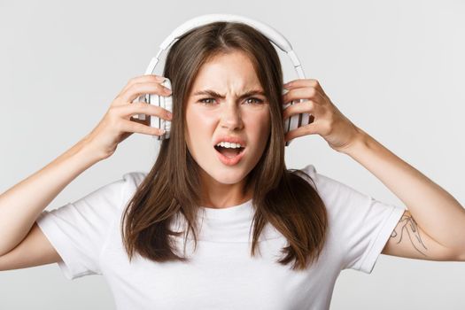 Close-up of angry and confident young girl complaining on awful music in wireless headphones, grimacing.