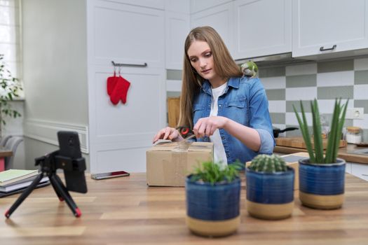 Woman recording video on smartphone moment of unpacking cardboard box. Showing purchases ordered on Internet, product quality reviews with followers, blog content, feedback. Pet parrot helping unpack