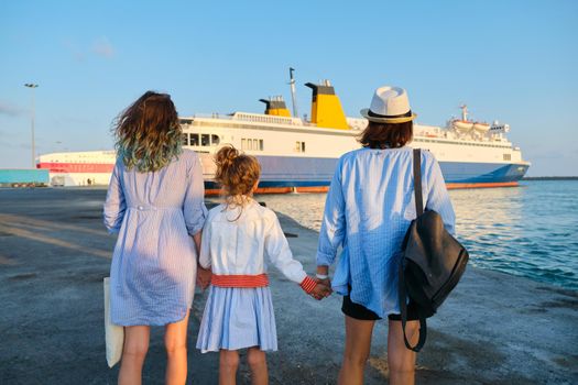Sea family vacation, mother and daughters in the seaport holding hands looking at the ferry