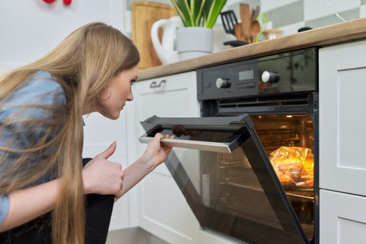 Cooking at home, roasting meat in oven, young woman putting marinated chicken in baking bag in oven, kitchen interior background