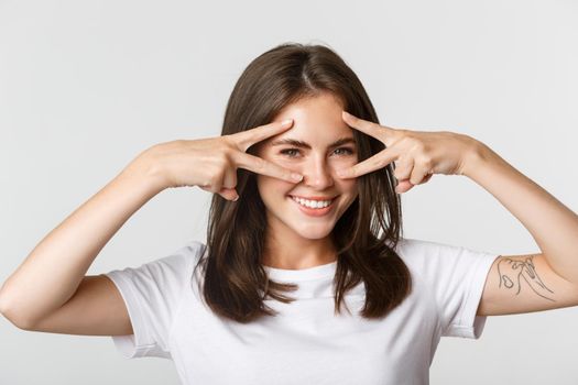 Close-up of sassy attractive brunette girl showing peace gestures over eyes and smiling happy.