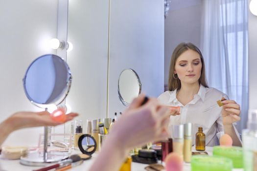 Young beautiful woman doing facial massage with silicone tools cosmetic vacuum jars, using massage oil. Female sitting at home at make-up table with mirror, caring for skin of face, home spa treatment