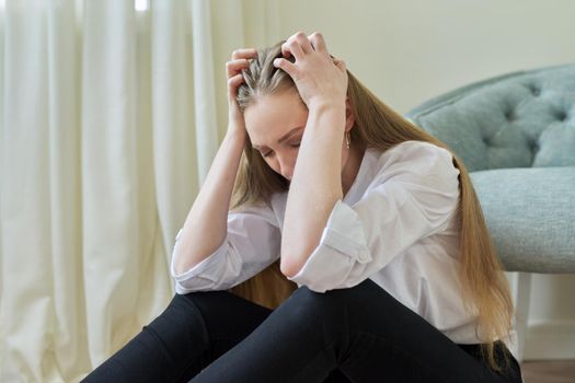 Upset crying young woman sitting at home on the floor. Negative emotions, stress, mental health, frustration, pain, people concept