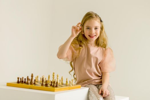 A very smart little girl holding a chess piece in her hand on a white background. The concept of the child's intellectual development, sports games.