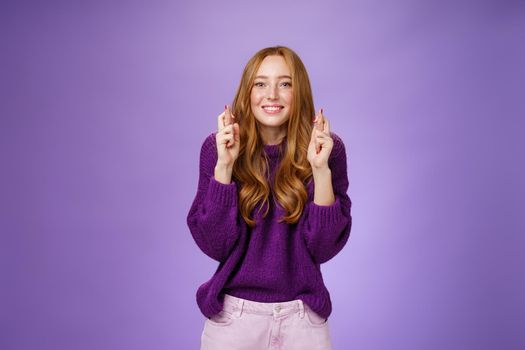 Optimistic happy girl wishing dream cope true, crossing fingers for good luck and smiling hopeful, supplicating wanting pray be heard standing joyful with anticipation over purple wall.