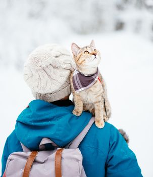 Traveler woman with cute cat on her shoulder walking in winter outdoor.