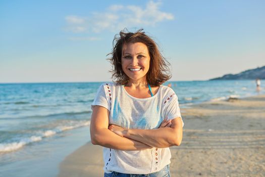 Portrait of happy smiling confident middle aged woman relaxing on sandy beach on sunny sunset day