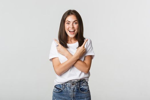 Excited beautiful girl looking amazed and pointing fingers sideways, showing two variants.