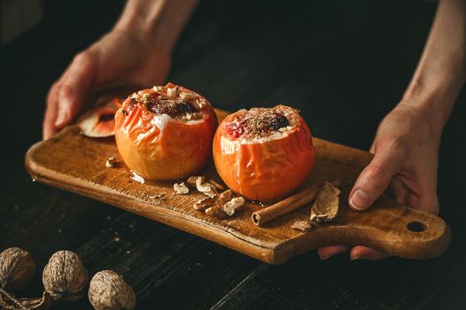 baked apples with cottage cheese with berries and nuts, topped with honey and sprinkled with cinnamon. on a wooden surface in a rustic style