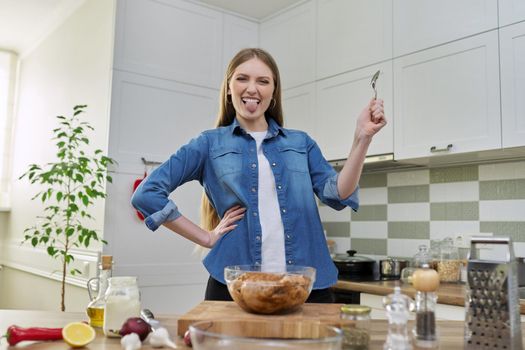 Young woman prepares chicken at home, marinates meat with spices in glass bowl on table, kitchen interior background, cook at home