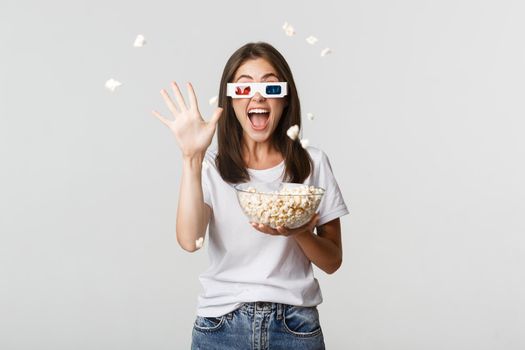 Joyful attractive young girl in 3d glasses, throwing popcorn at screen while watching movie.