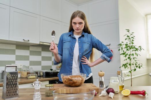 Young woman prepares chicken at home, marinates meat with spices in glass bowl on table, kitchen interior background, cook at home