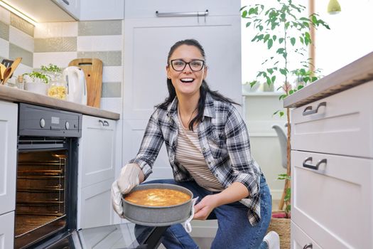 Woman at home in kitchen taking out hot apple pie from oven. Cooking at home, homemade baking, eating at home, lifestyle, hobbies and leisure