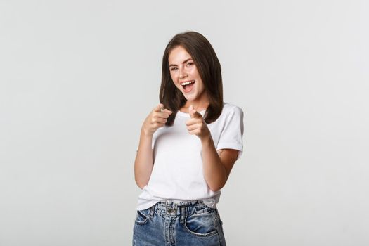 Smiling cheerful brunette girl pointing finger at camera, congratulate you, praising good choice.