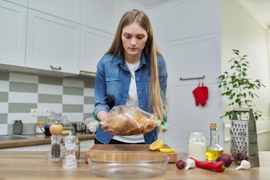 Young woman cooking baked chicken in baking sleeve with spices, kitchen interior background, cooking at home concept