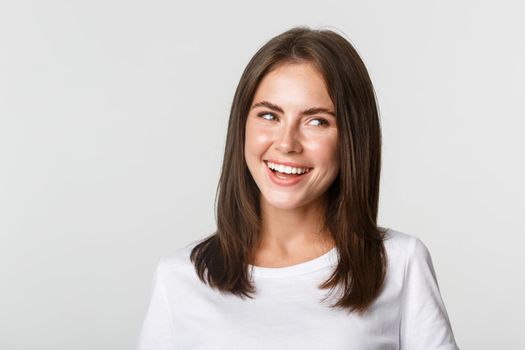 Close-up of joyful beautiful brunette girl looking right and laughing happy, white background.