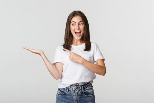 Attractive young woman pointing finger at something she holding on hand.