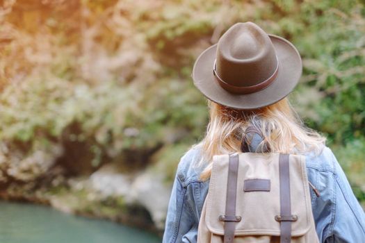 Traveler woman wearing in a hat and jeans jacket walking in nature outdoor, rear view.