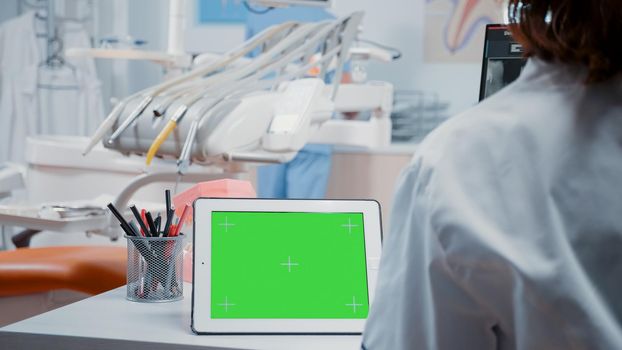 Close up of digital tablet with horizontal green screen on desk in dentistry cabinet. Dentist analyzing isolated template and mockup background with chroma key for stomatological care