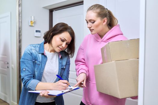 Online shopping delivery service, courier young woman with cardboard boxes near front door in apartment, adult woman buyer takes boxes