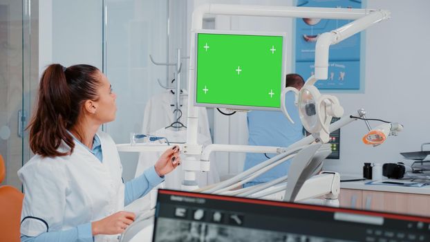Woman analyzing green screen on monitor and teeth x ray for dental examination. Dentist using chroma key and mockup display for checkup while looking at radiography for oral care