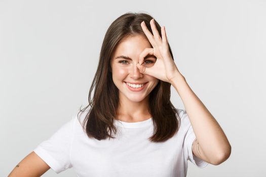 Close-up of attractive confident girl smiling satisfied and showing okay gesture over eye.