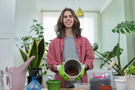 Green eco hobby of young male, teenager showing plant, soil, expanded clay, soil additives perlite vermiculite at camera, recording video for plant vlog blog. Eco green trends, modern city apartments