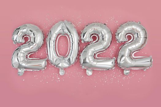 Silver foil balloons numeral 2022 and confetti on pink background Happy New year 2022 celebration Flat lay