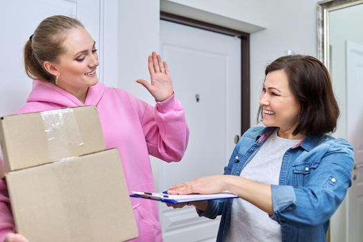 Online shopping delivery service, courier young woman with cardboard boxes near front door in apartment, adult woman buyer takes boxes