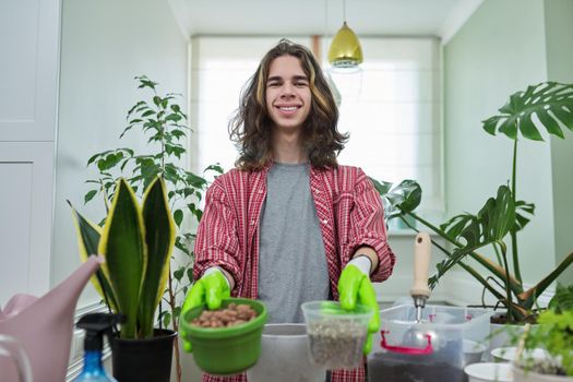 Green eco hobby of young male, teenager showing plant, soil, expanded clay, soil additives perlite vermiculite at camera, recording video for plant vlog blog. Eco green trends, modern city apartments