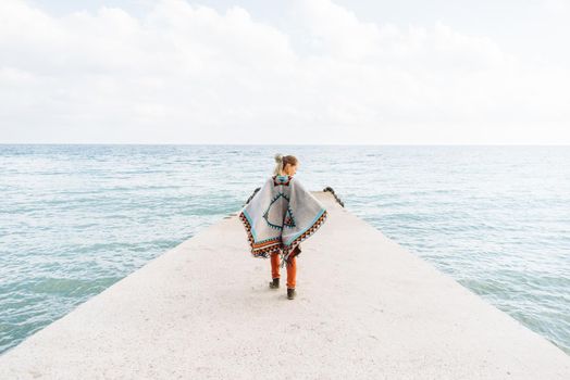 Beautiful boho style woman walking on sea pier.